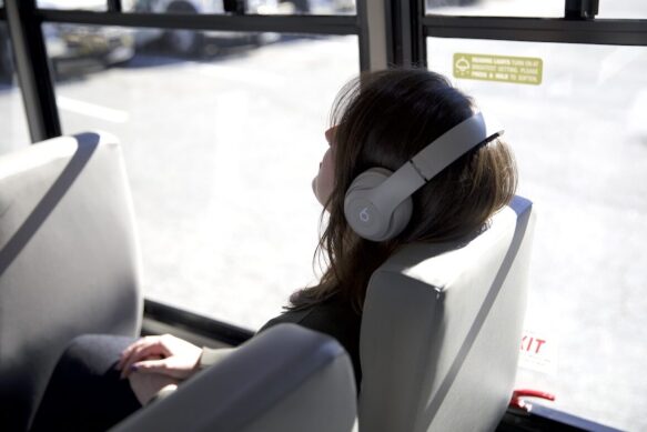 A rider relaxing on the bus listening to music, since they don't have to drive themselves