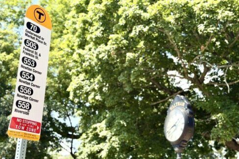 MBTA Bus Stop Sign showing routes including Express Route 505, with Waltham Center clock in the background